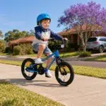 Four-year-old boy wearing a blue helmet and happily pedalling a blue Kidvelo Rookie 14 through an Australian neighbourhood.