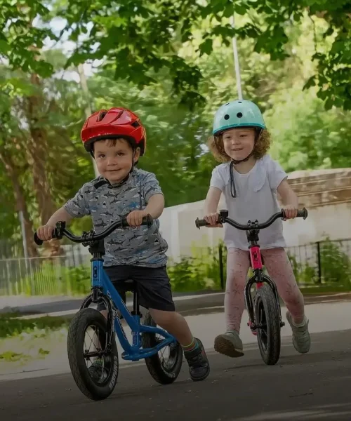 two kids boy and the girl, aging 2-3 riding balance bikes